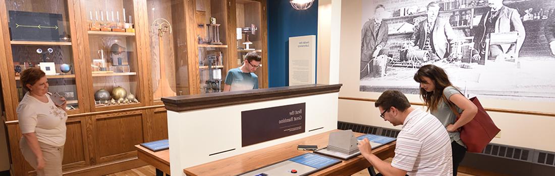 Museum visitors gathered around an interactive display. Two are interacting with the display and two others are watching from a short distance